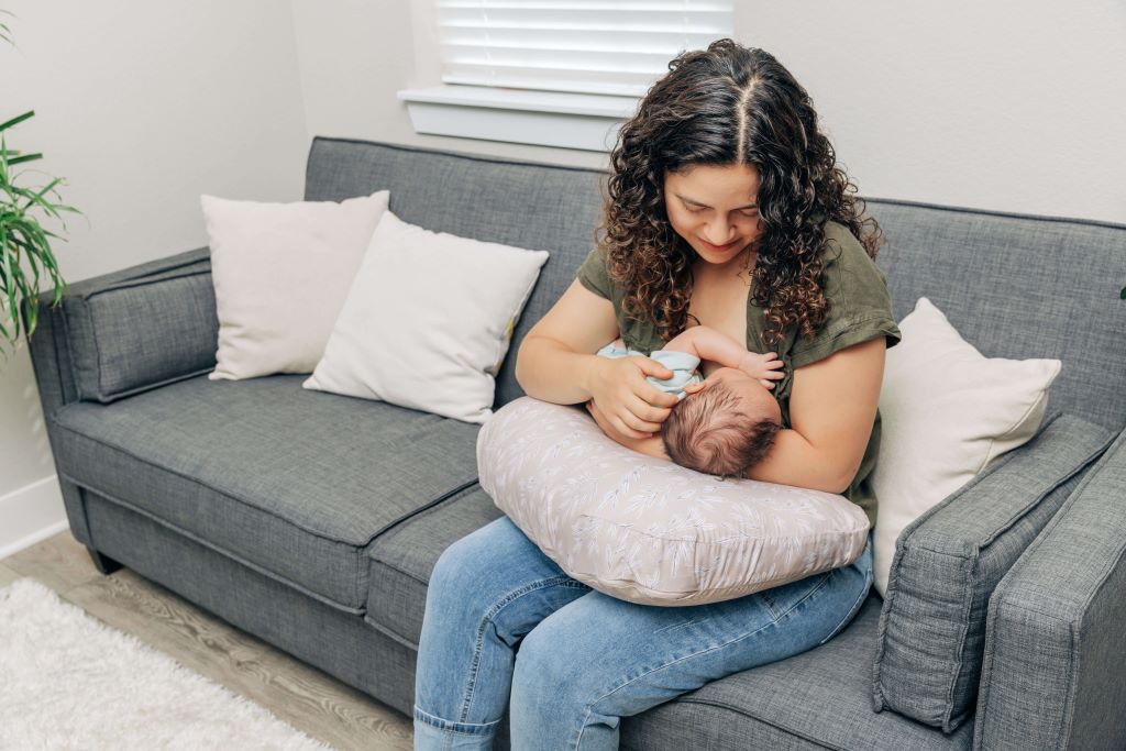 New mom holding baby with supportive breastfeeding pillow during feeding